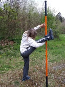 Frau hebt Bein und hält sich an einem Stab fest