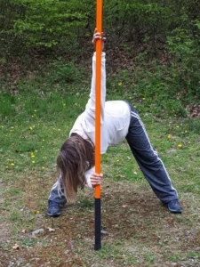 Frau in weiter Grätsche, dreht sich mit Stab nach oben