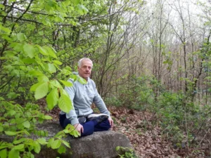 Mann sitzt meditierend auf einem Felsen im Wald