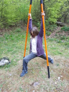 Frau in weiter Grätsche, mit erhobenen Armen an zwei Stäben