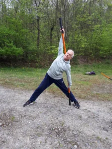 Mann streckt Arm nach oben mit Stab, seitliche Dehnung