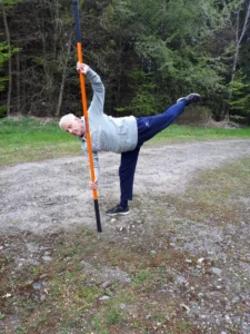 Mann mit ausgestrecktem Bein in Balancehaltung mit Stab